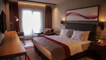 Quarto de hotel com uma cama grande, uma escrivaninha, uma cadeira, uma televisão e um quadro na parede.