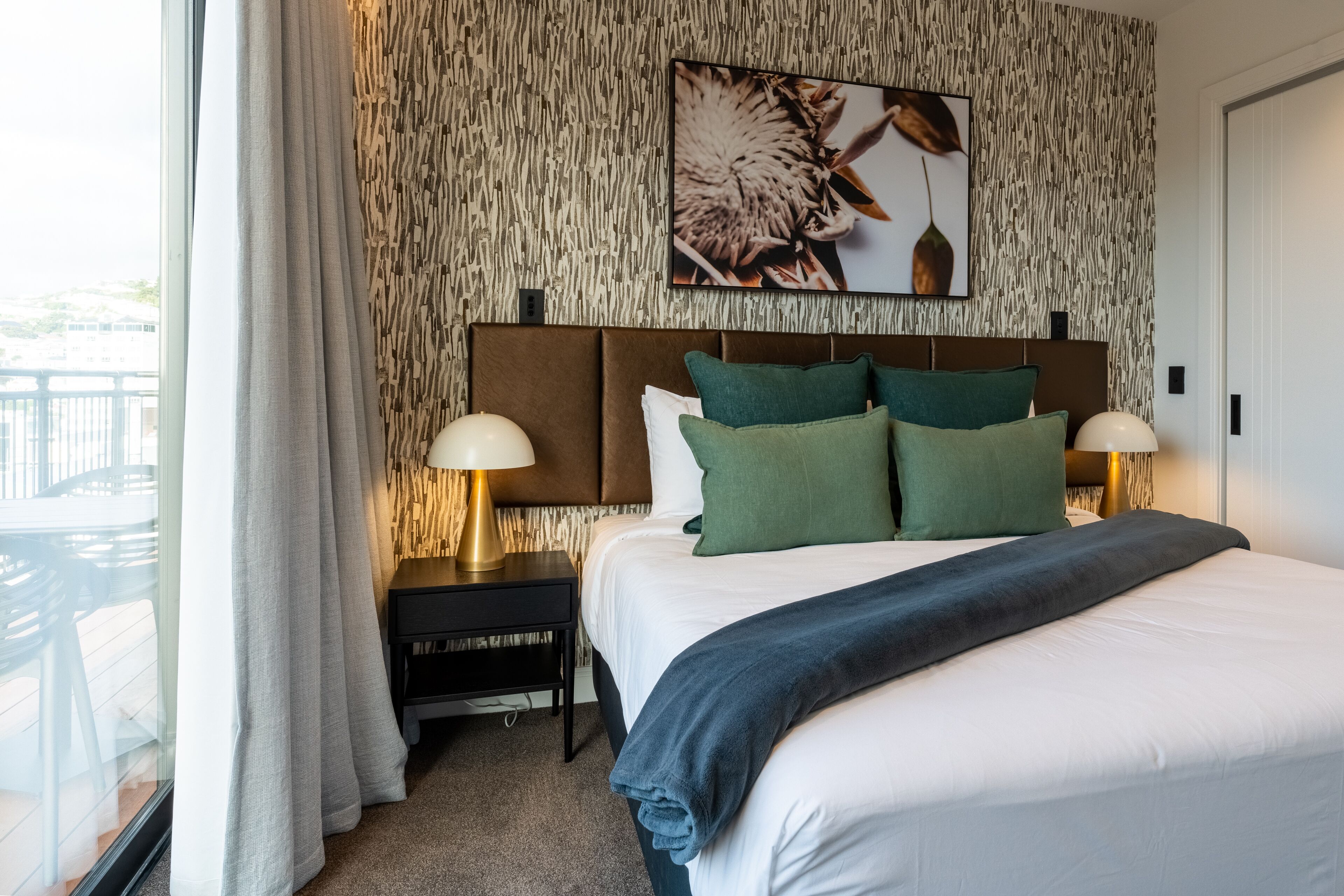 Habitación de hotel con una cama grande, dos mesitas de noche con lámparas, un cuadro en la pared y vistas por la ventana.