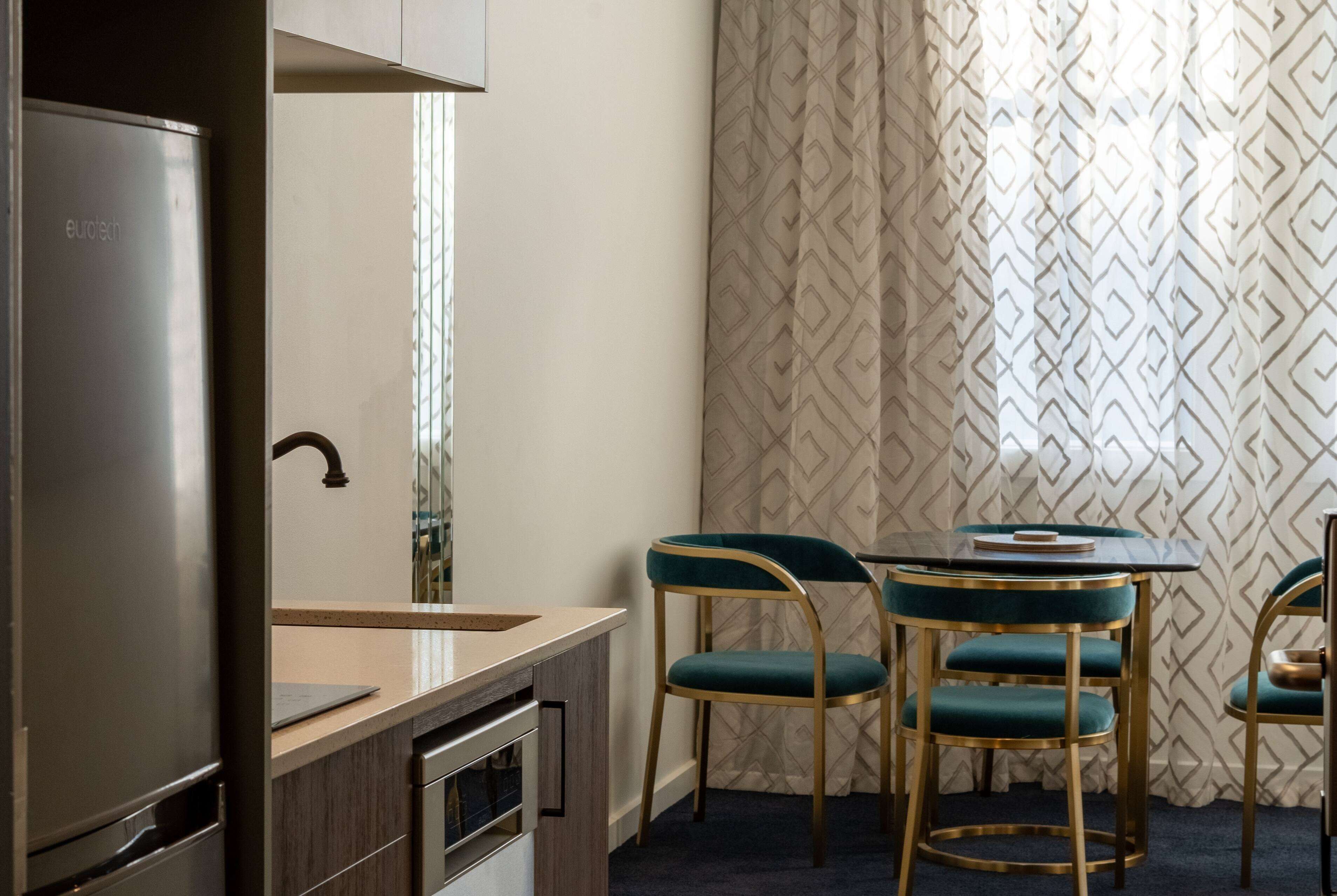 A compact kitchen with a refrigerator, a sink, and a small countertop. There are two chairs with a unique design and a table with a decorative item on it.