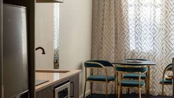 A compact kitchen with a refrigerator, a sink, and a small countertop. There are two chairs with a unique design and a table with a decorative item on it.