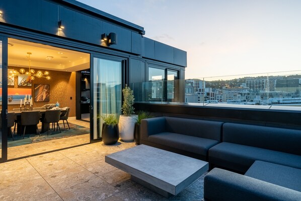 A modern outdoor seating area with a sofa and a coffee table, a dining area with a table and chairs, and a view of the cityscape. - TRYP by Wyndham Wellington, Tory Street (Wellington)