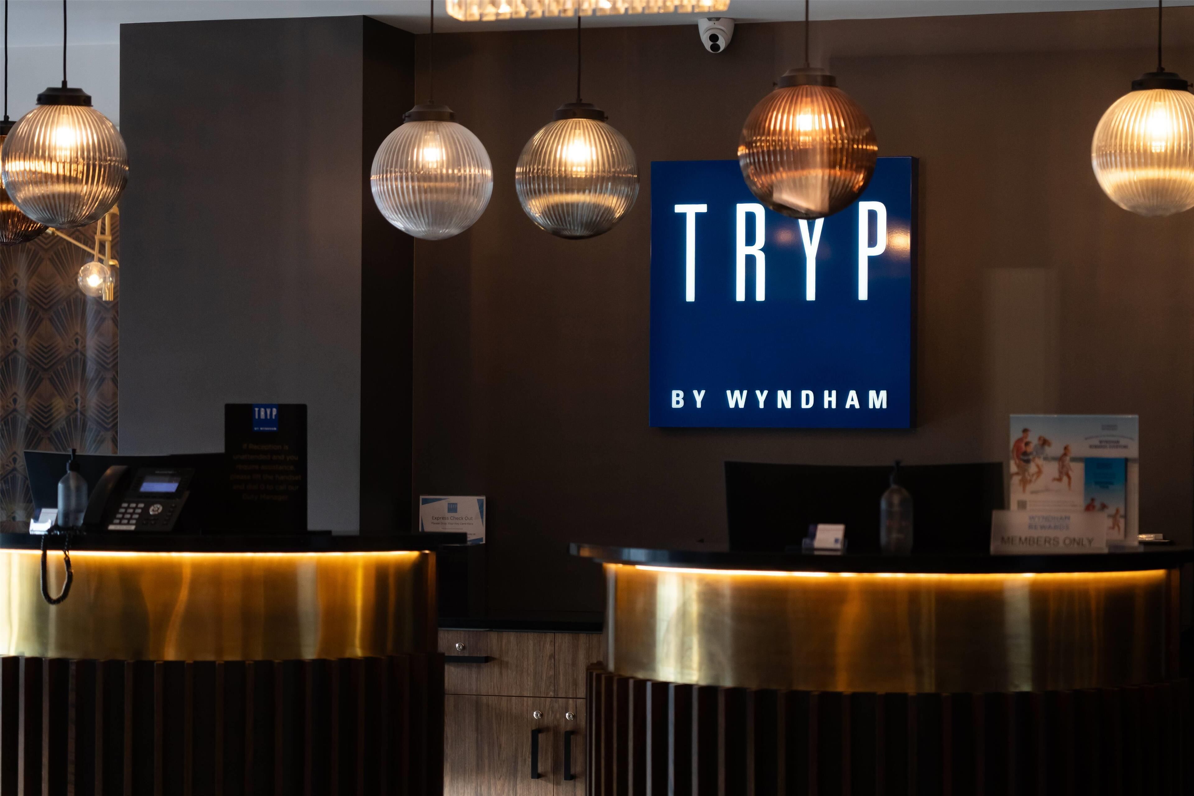 Una recepción con un letrero azul que dice "TRYP BY WYNDHAM" y una cámara de seguridad en la parte superior.