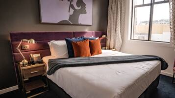 A hotel room with a large bed, a nightstand with a lamp, a telephone, and a painting on the wall.