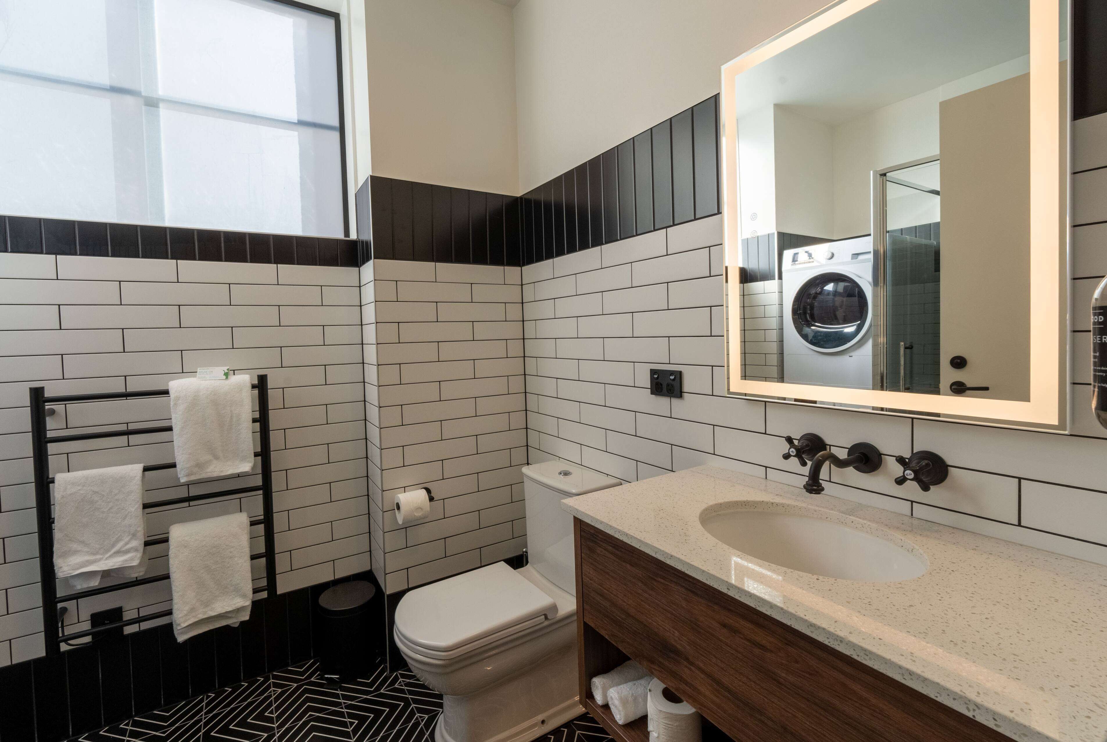 A modern bathroom with a white toilet, black and white tiled walls, a wooden vanity, and a large mirror.