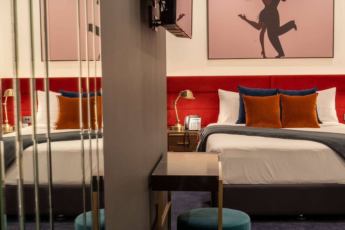 A hotel room with two beds, red headboards, and a small table with a lamp.