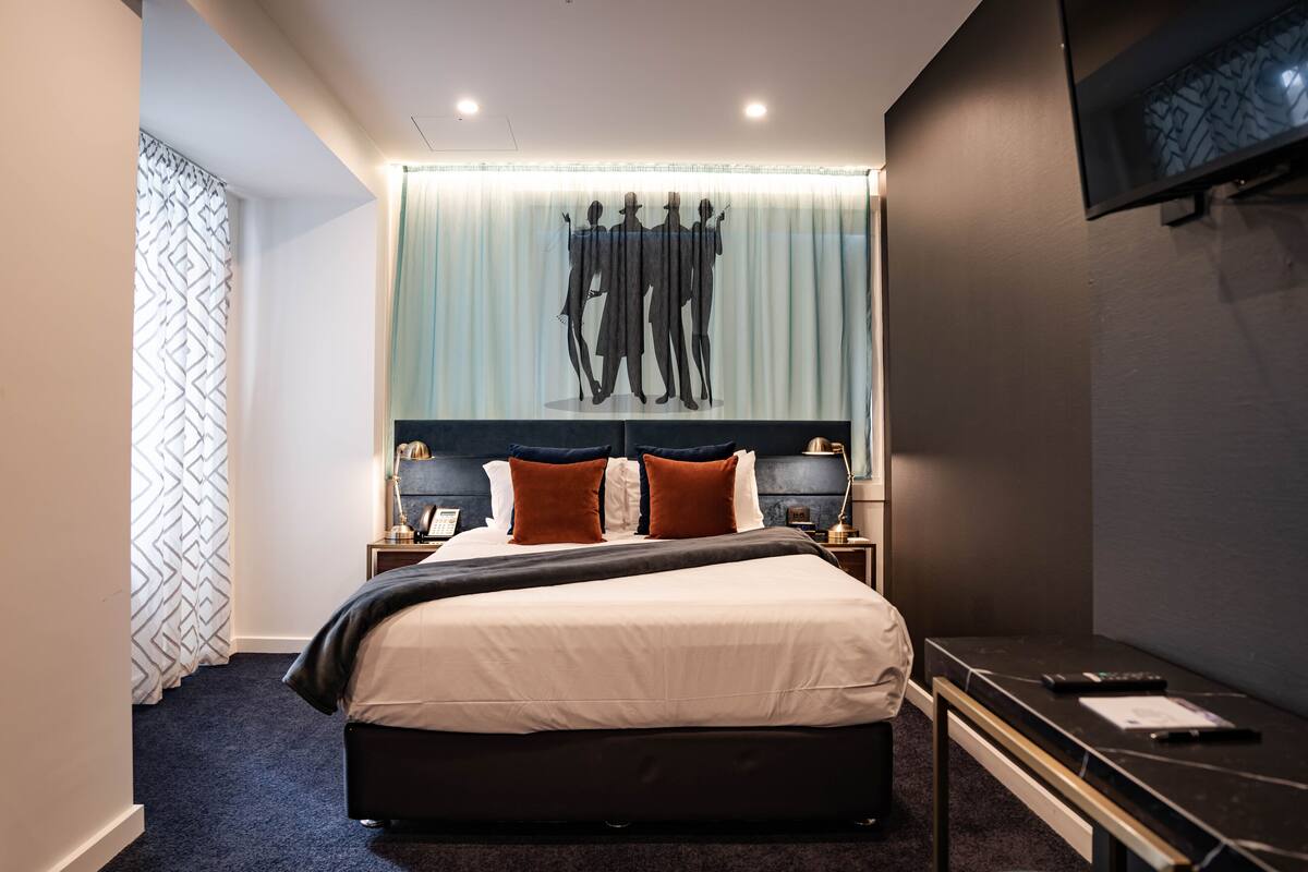 A modern hotel room with a large bed, a desk, and a TV mounted on the wall.