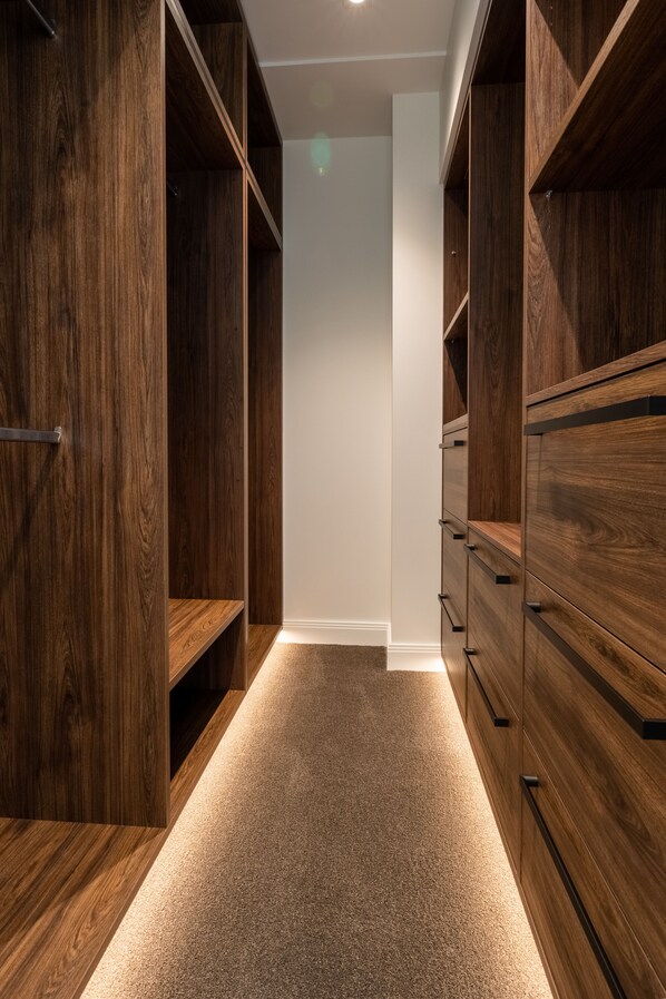A narrow walk-through closet with wooden shelving and drawers, carpeted floor, and recessed lighting. - TRYP by Wyndham Wellington, Tory Street (Wellington)