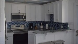 Una cocina con armarios blancos, microondas, horno, cafetera y fregadero.