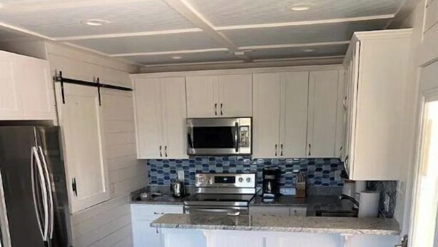 Cocina compacta con armarios blancos, microondas, estufa y refrigerador. Hay dos taburetes de madera en la barra.