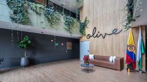 A modern lobby with a wooden reception desk, a sofa, and a coffee table. There are potted plants and flags on display.