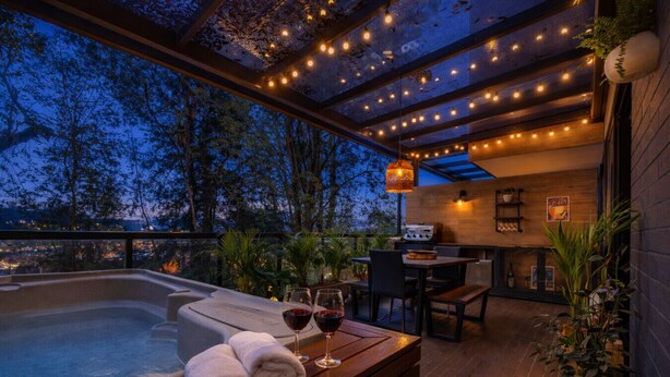 An outdoor hot tub area with a wooden deck, a table with towels and wine glasses, and string lights.