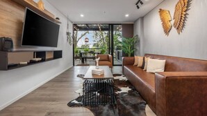 A modern living room with a large flat-screen TV, a leather sofa, a coffee table, and a cowhide rug.