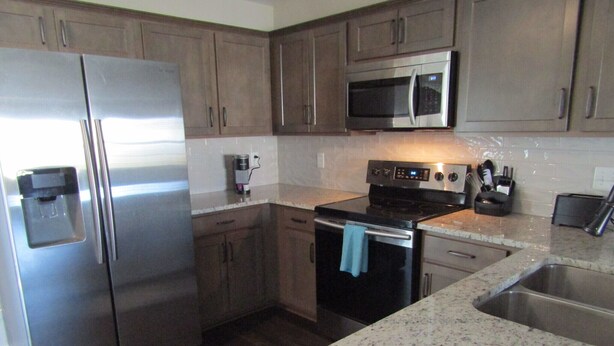 A modern kitchen with stainless steel appliances, wooden cabinets, and a granite countertop. - Cheerful 2-Bedroom Townhouse with Pool (Clarksville)