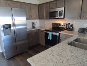 A modern kitchen with stainless steel appliances, wooden cabinets, and a granite countertop.
