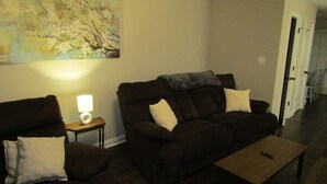 A living room with two dark brown sofas, a small wooden coffee table, and a lamp on a side table. A large abstract painting is on the wall. - Cheerful 2-Bedroom Townhouse with Pool (Clarksville)