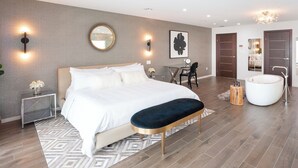 A modern bedroom with a large bed, bedside tables, a desk, and a bathroom with a bathtub. - Luxury 6 Bedroom Villa on the Beach in Bodden Town (Breakers)