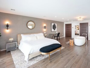 Ein modernes Schlafzimmer mit einem großen Bett, Nachttischen, einem Schreibtisch und einem Badezimmer mit einer Badewanne.