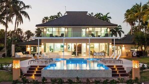A two-story house with a swimming pool, outdoor seating, and palm trees. - Luxury 6 Bedroom Villa on the Beach in Bodden Town (Breakers)