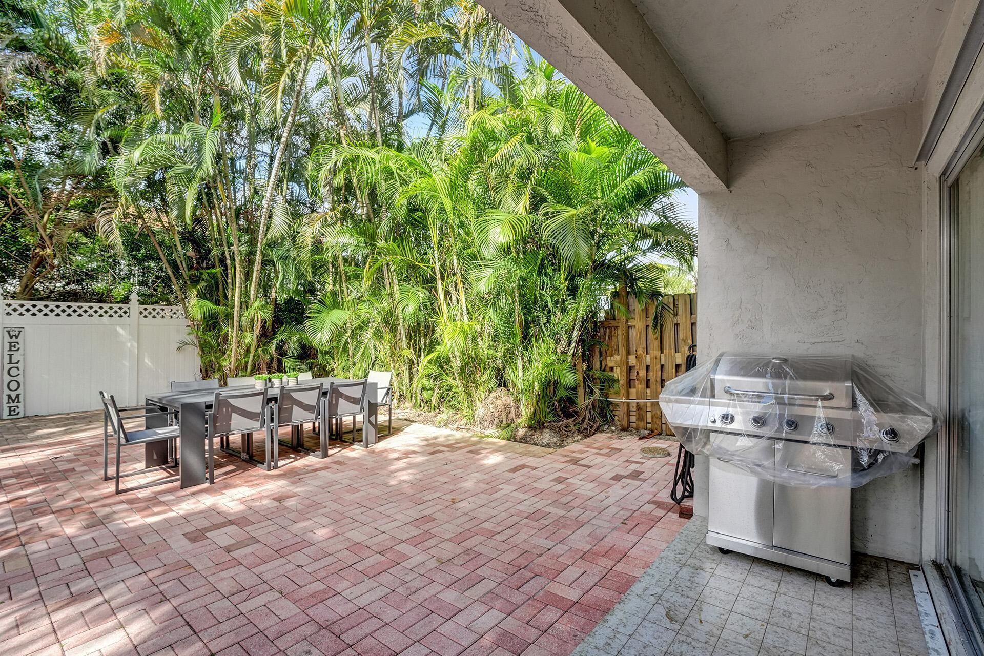 A patio with a grill, outdoor seating, and lush greenery.