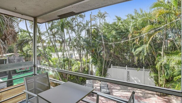 Ein Balkon mit Glasgeländer, der auf einen Garten mit Palmen und einem Pflasterweg blickt.