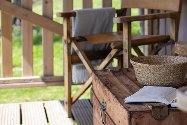 Außenpatio des Lodge Comet mit rustikalem Charme und dezenter Eleganz. Die Holzterrasse, klassische Sitzmöbel und handwerkliche Details schaffen einen intimen Bereich für Ruhe und Entspannung. Ein privater Rückzugsort im Grünen, geprägt von Licht, Stille und Natur in der Wilderness.
