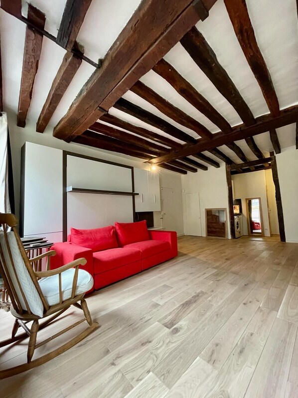 Un salon spacieux avec un canapé rouge, un plancher en bois et des poutres apparentes en bois au plafond.
