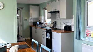Een compacte keuken met een eethoek, inclusief een klein eiland, witte kastjes en een raam met gordijnen.