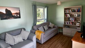 Een woonkamer met twee grijze banken, een boekenkast en een schilderij aan de muur.