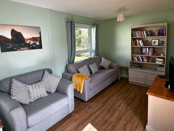 Uma sala de estar com dois sofás cinzentos, uma estante de livros e um quadro na parede.