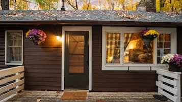 Cozy cabin with a welcoming front door, small porch, and two windows adorned with flower baskets.