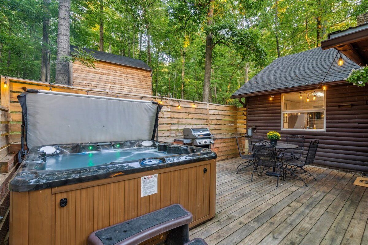 A wooden deck with a hot tub, barbecue grill, and outdoor seating area surrounded by trees.
