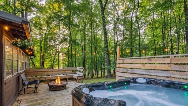Un jacuzzi rodeado de mobiliario de madera para terraza, un brasero y una valla de madera.