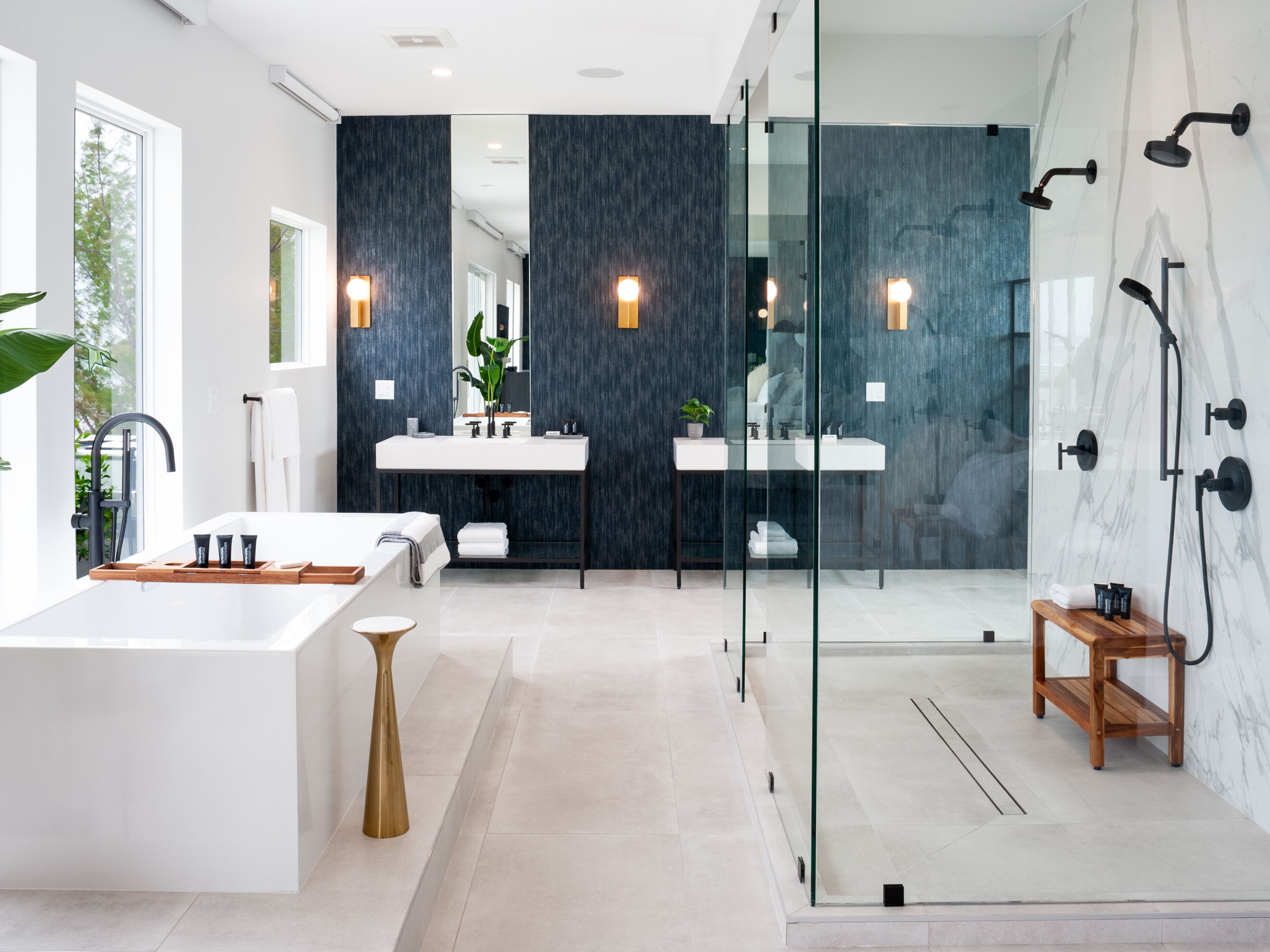 Un baño moderno con una bañera grande, dos lavamanos, una cabina de ducha de vidrio y un banco de madera.