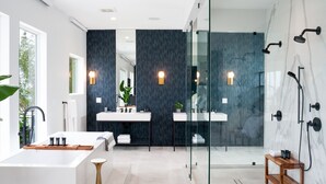 Ein modernes Badezimmer mit einer großzügigen Badewanne, zwei Waschbecken, einer Duschkabine aus Glas und einer Holzbank.
