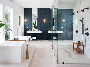 Ein modernes Badezimmer mit einer großzügigen Badewanne, zwei Waschbecken, einer Duschkabine aus Glas und einer Holzbank.