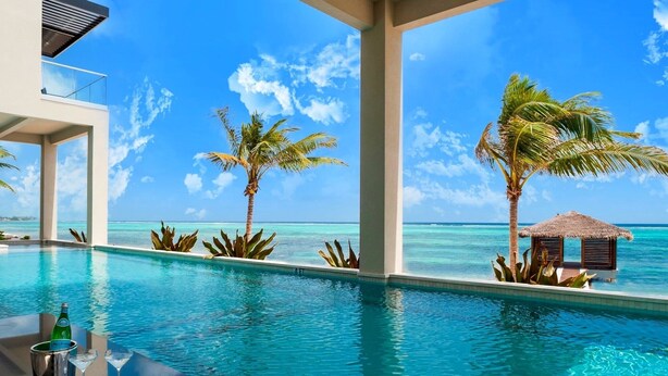 Ein Pool mit klarem, blauem Wasser, Palmen und Blick auf den Ozean.