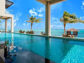 Ein Pool mit klarem, blauem Wasser, Palmen und Blick auf den Ozean.