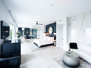 Ein modernes Schlafzimmer mit einem großen Bett, einem Fernseher, einem Duschbad mit Glastüren und einem weißen Sofa.