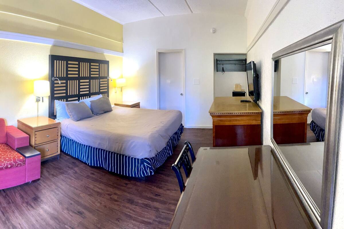 Une chambre d’hôtel avec un lit, un canapé rouge, une table de chevet en bois, un bureau et un miroir.