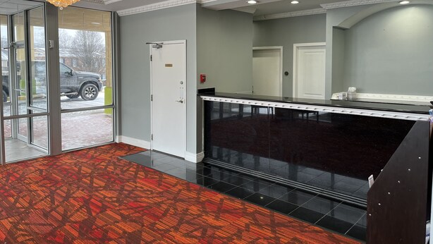 A hotel lobby with a reception desk, a patterned carpet, a chandelier, and a door leading outside. - Hotel M Morgantown - WVU Area (Morgantown)