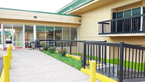 A building entrance with a glass door, a concrete pathway, and a yellow bollard. - Hotel M Morgantown - WVU Area (Morgantown)