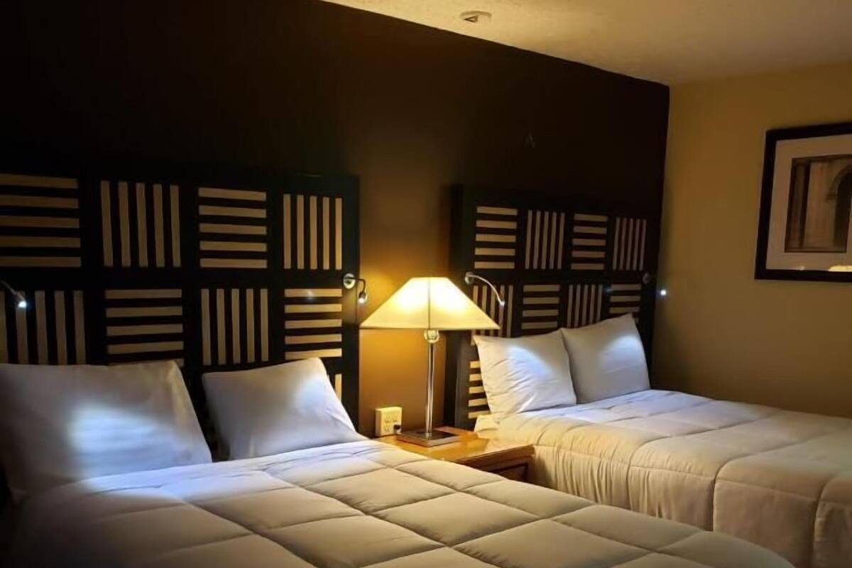 Une chambre d’hôtel avec deux lits, une table de chevet avec une lampe et un luminaire fixé au mur.