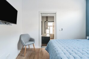 Un dormitorio con una cama, una silla y un televisor montado en la pared.