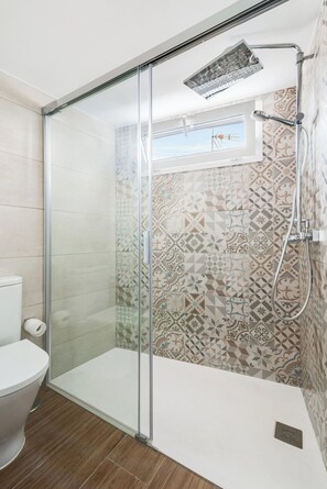 Un baño moderno con ducha acristalada, azulejos estampados y ventana visible.
