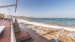 A coastal walkway with steps leading to the beach, a clear sky, and distant hills.