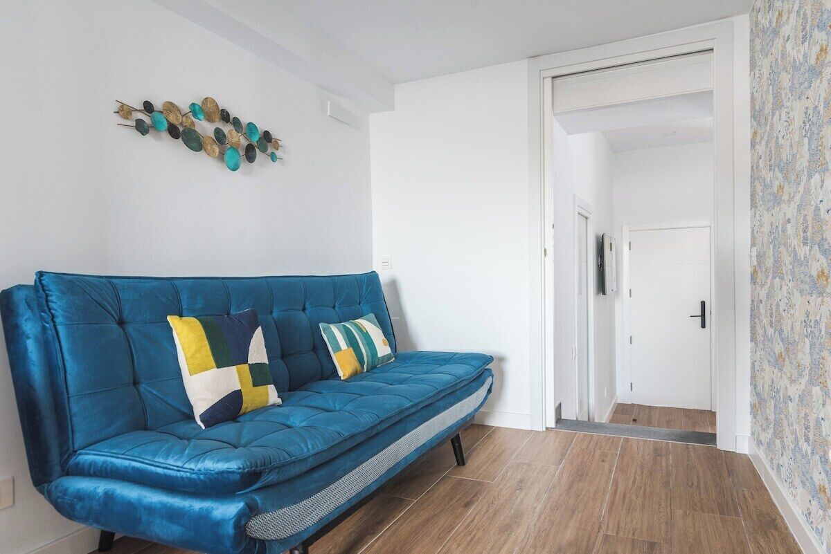 A blue sofa with patterned cushions in a room with wooden flooring and a white door.