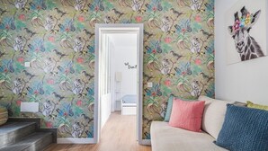 A room with a colorful floral wallpaper, a sofa with colorful cushions, and a framed picture of a giraffe on the wall.