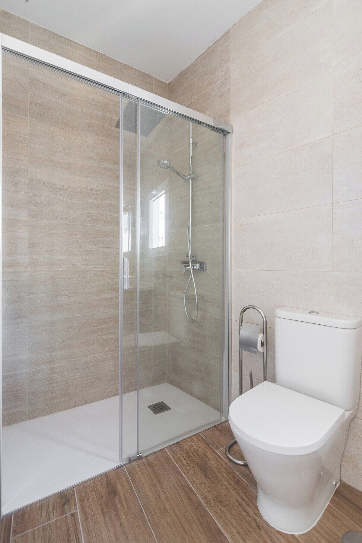 A modern bathroom with a glass-enclosed shower, a toilet, and tiled walls.
