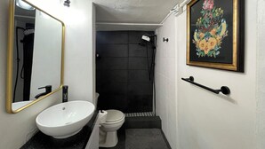 Ein Badezimmer mit weißem Waschbecken, WC und Dusche. An der Wand hängt ein gerahmtes Blumenbild und ein Spiegel mit goldener Rahmung.