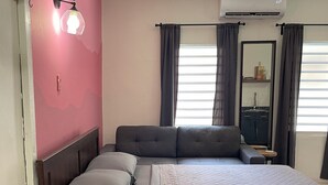 Ein modernes Schlafzimmer mit Bett, Nachttisch, einem kleinen Hocker, einem Fenster mit Vorhängen und einer Klimaanlage.